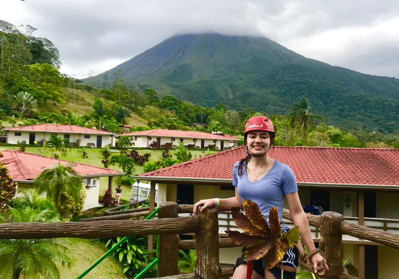 女孩穿着滑索装备，背景是房子和火山